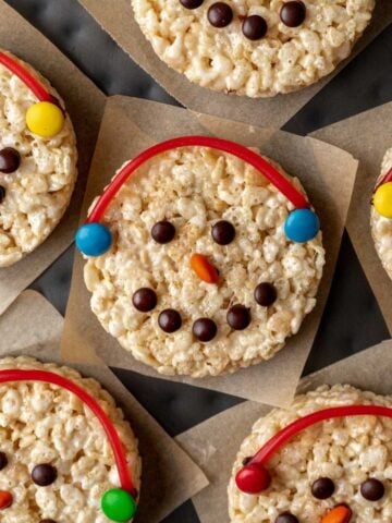 Snowman rice krispie treats decorated with colored candies and a candy string earmuffs.