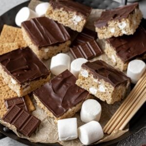Smores rice krispie treats on a serving platter with big marshmallows, hersheys chocolate, and graham crackers.