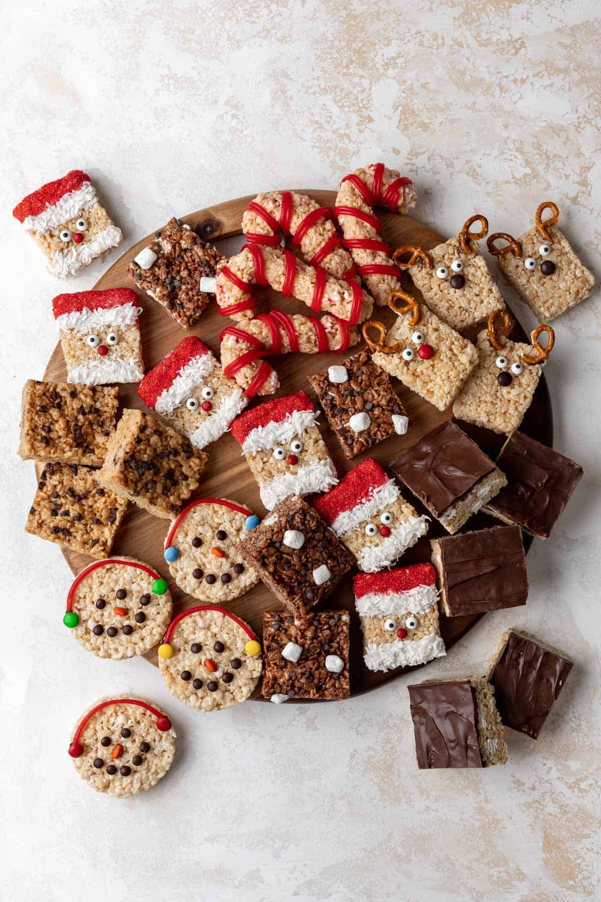 Holiday rice krispie treats dessert board with reindeer, santas, candy canes, snowmen, peanut butter, smores, and hot chocolate rice krispie treats.