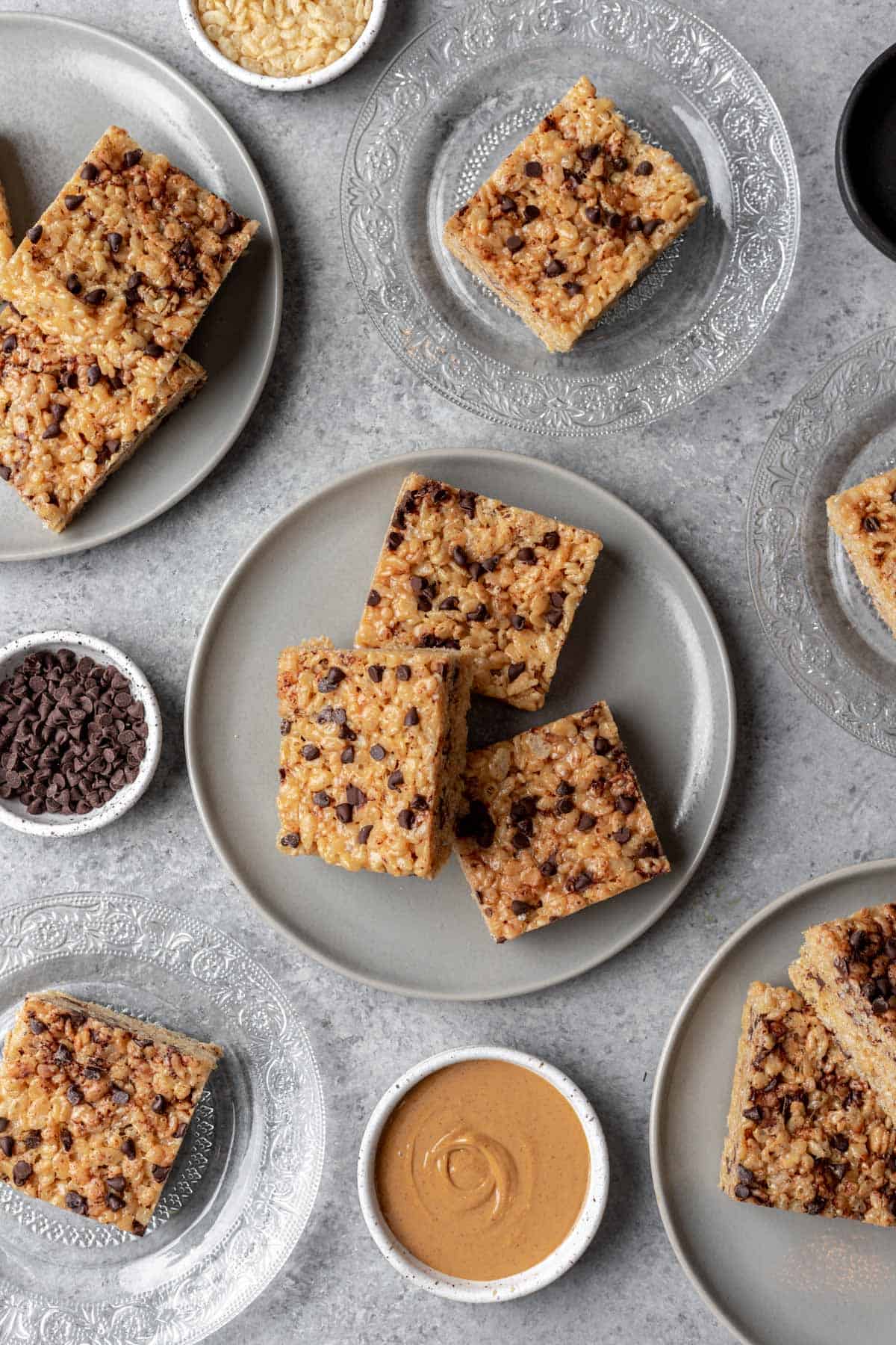 Peanut butter chocolate chip rice krispie treats on gray plates with a side of extra peanut butter and chocolate chips.