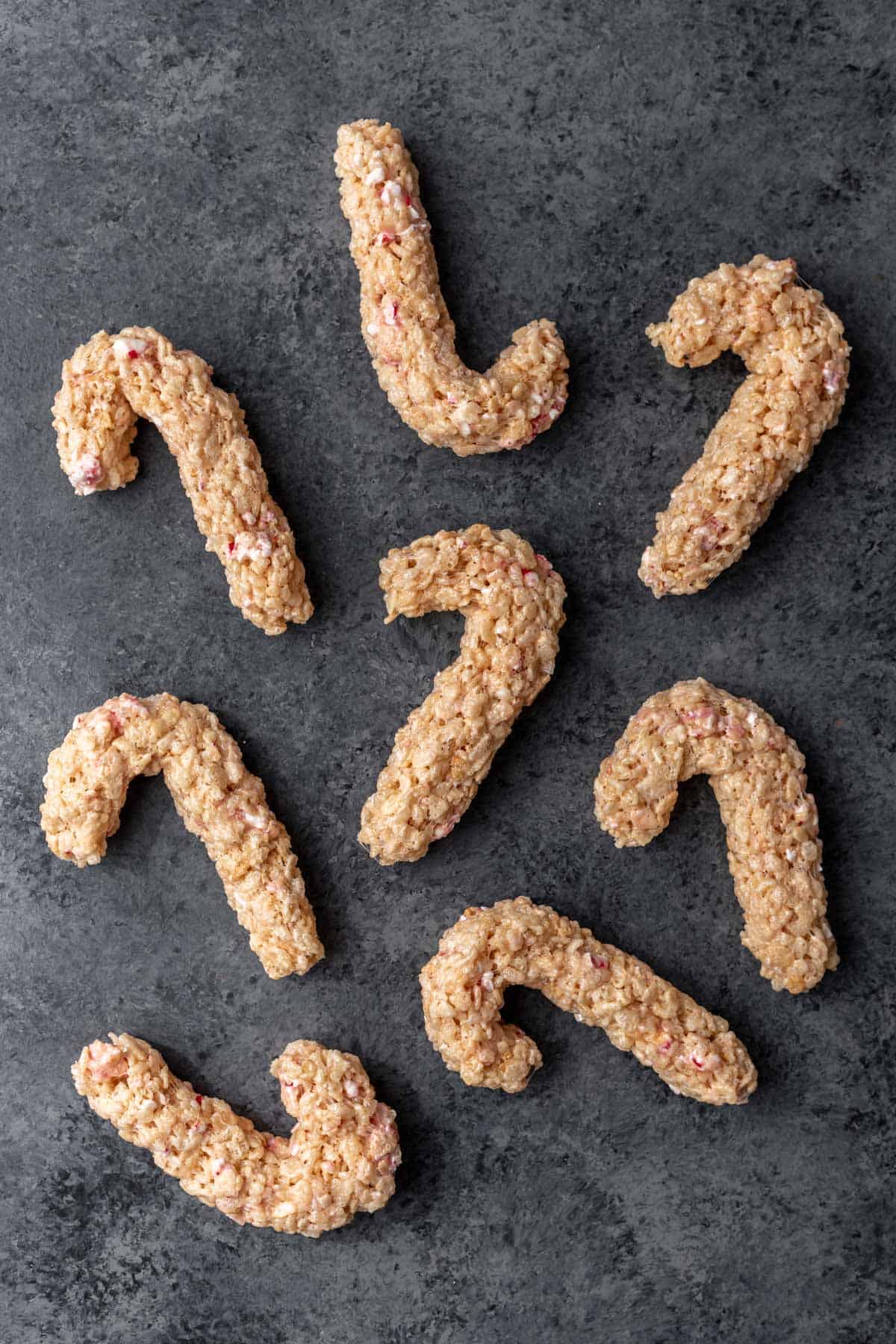 Rice krispie treats shaped as candy canes on a gray backdrop.