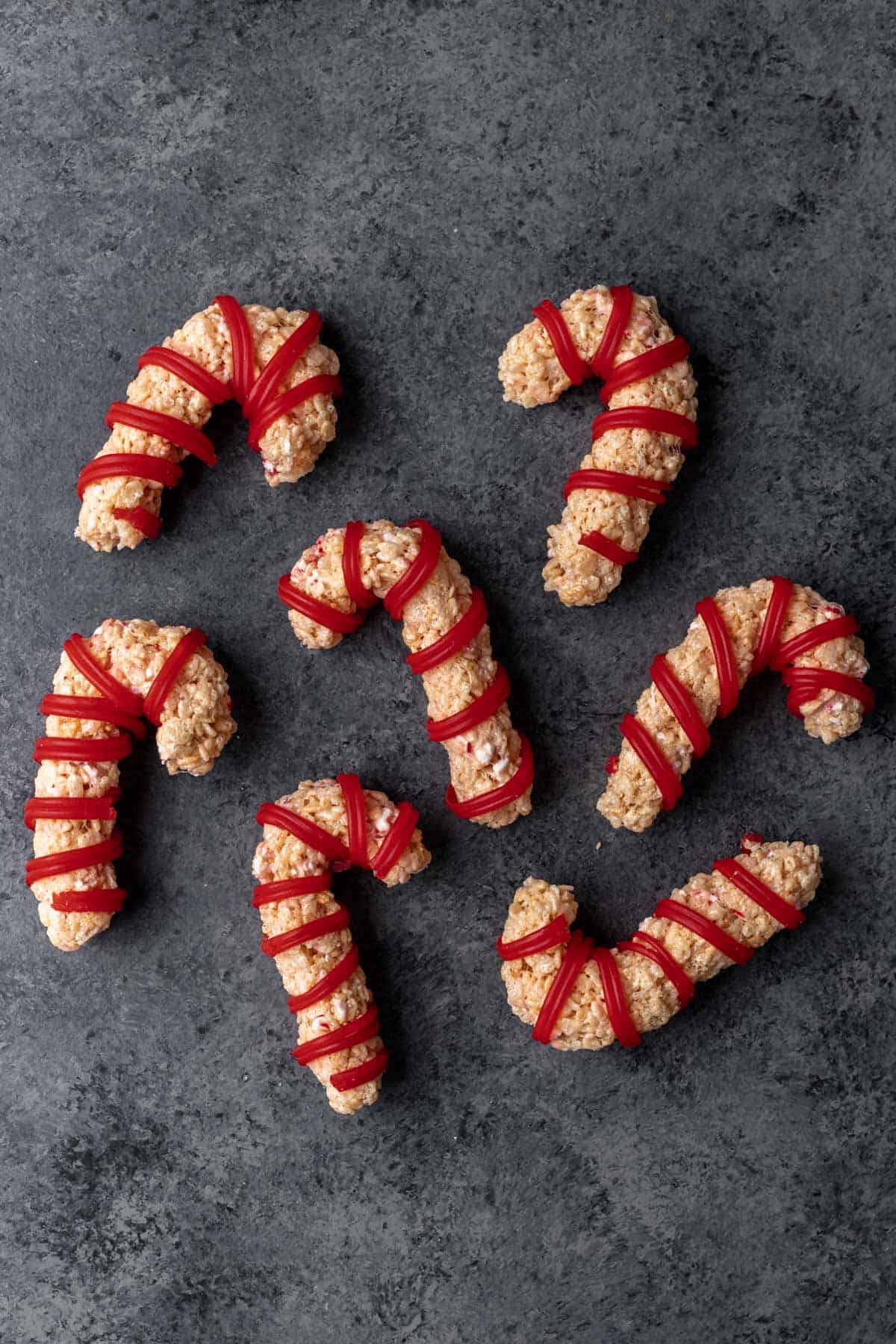 Candy cane shaped rice krispie treats wrapped in red candy strings.