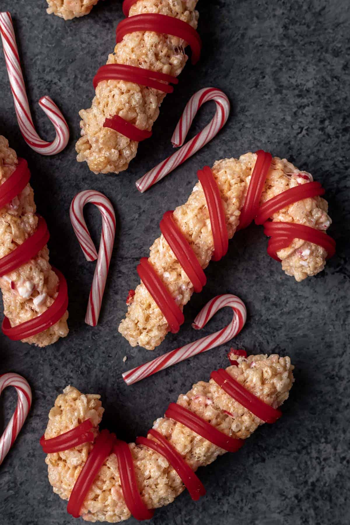 Peppermint candy cane rice krispie treats arranged on a dark gray backdrop with small candy canes around them.