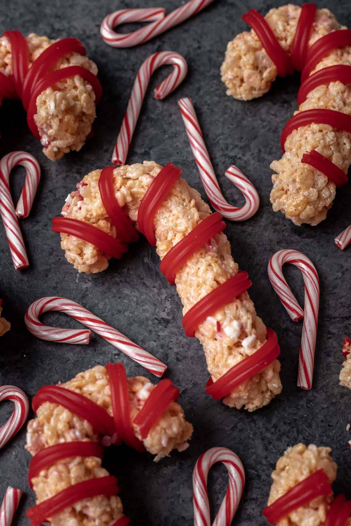 Peppermint candy cane rice krispie treats on a dark gray backdrop with small candy canes around it.