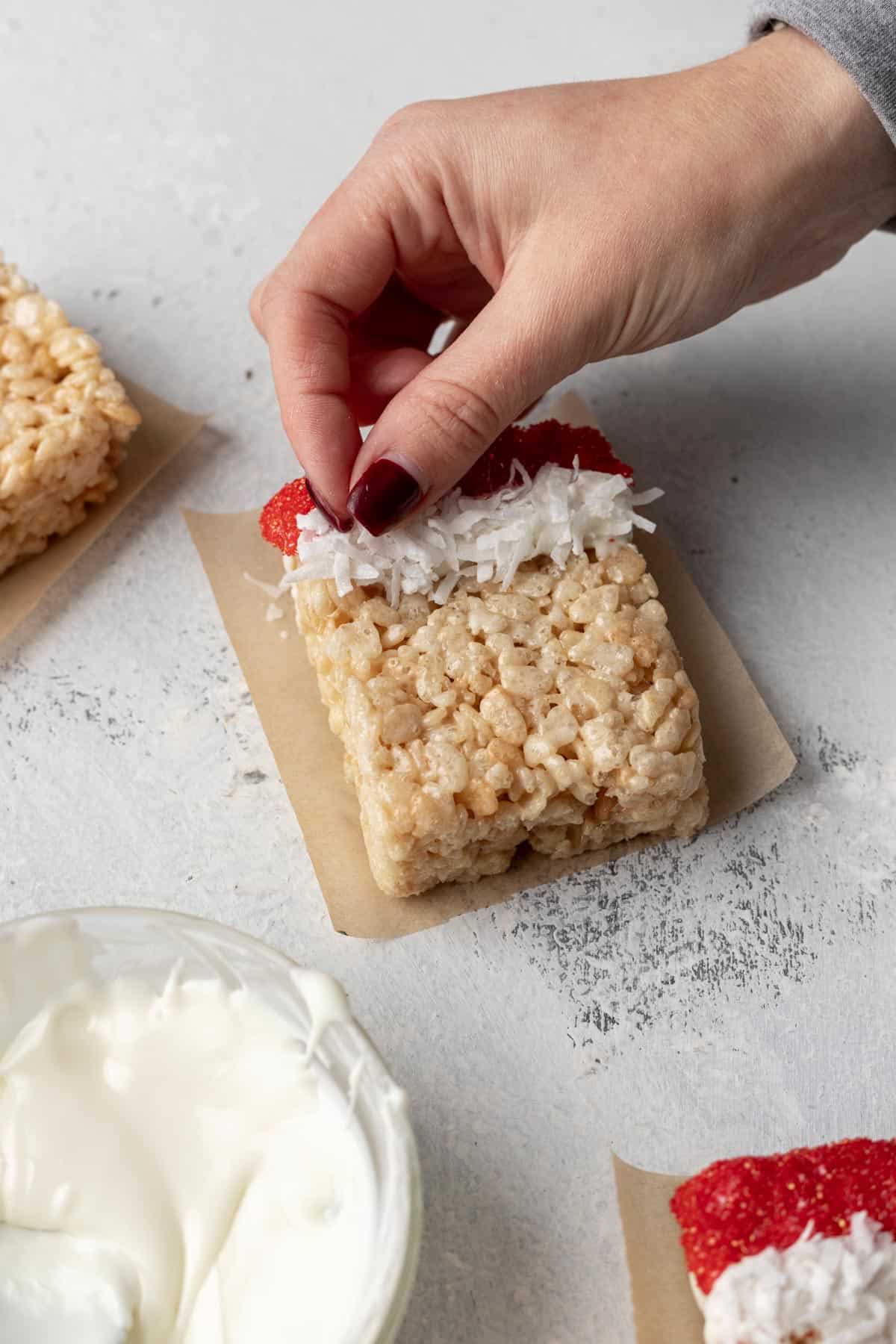 A hand placing coconut on top of melted white chocolate for santa's hair.
