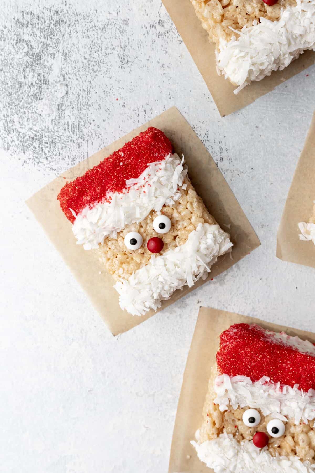 Santa rice krispie treat on parchment paper with candy eyes, red sugar hat, and a coconut beard.