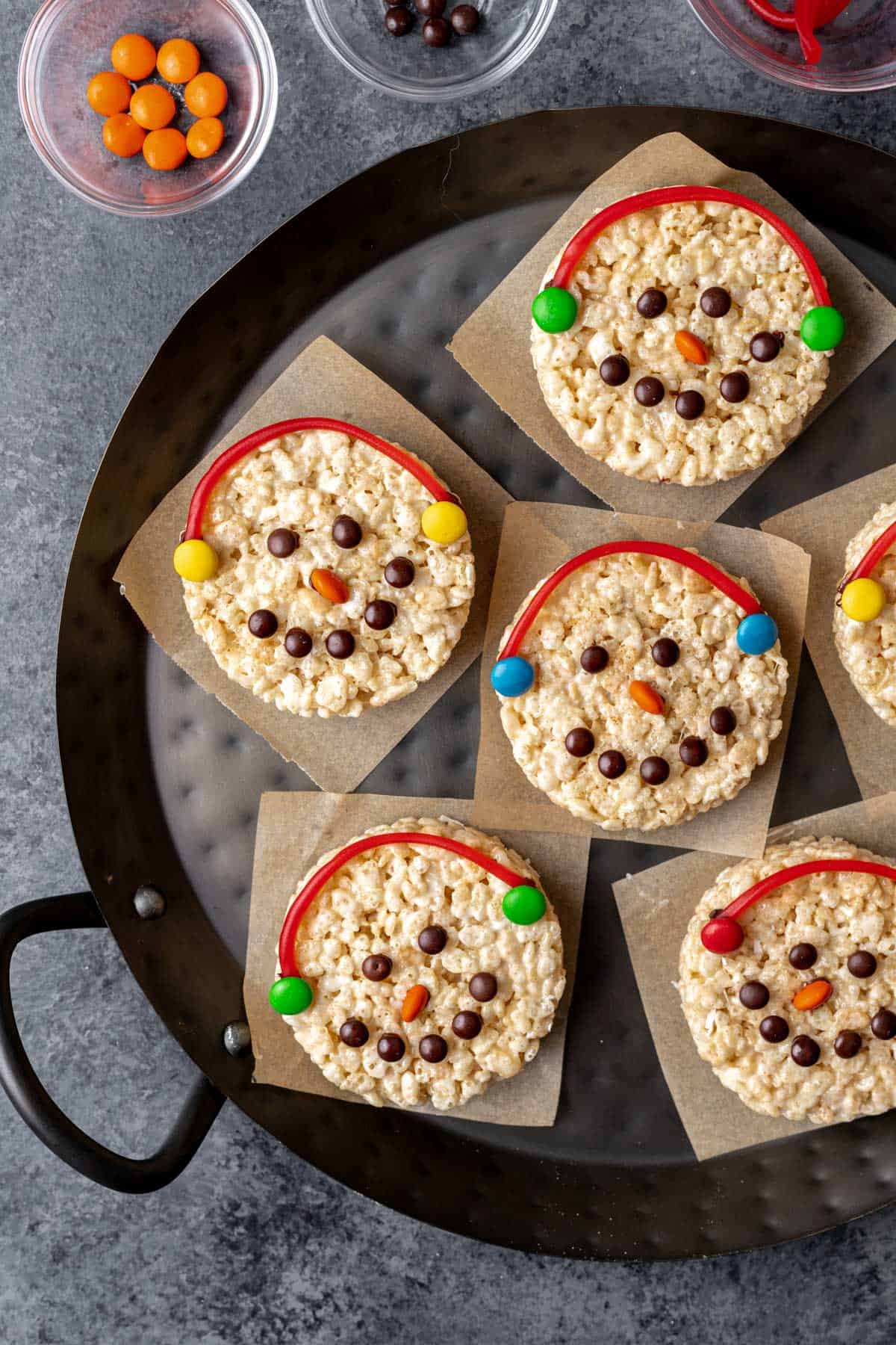 Snowman rice krispie treats colorfully decorated with candy on a serving tray.