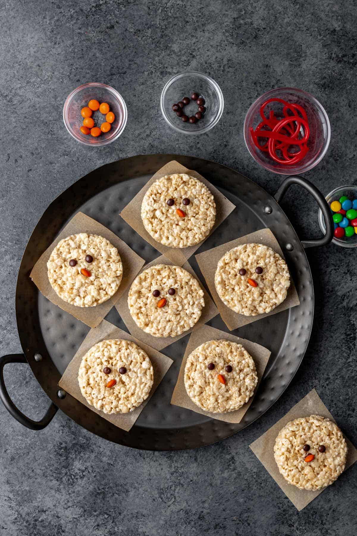 Circular rice krispie treats on a serving tray with brown candy eyes and orange candy noses.