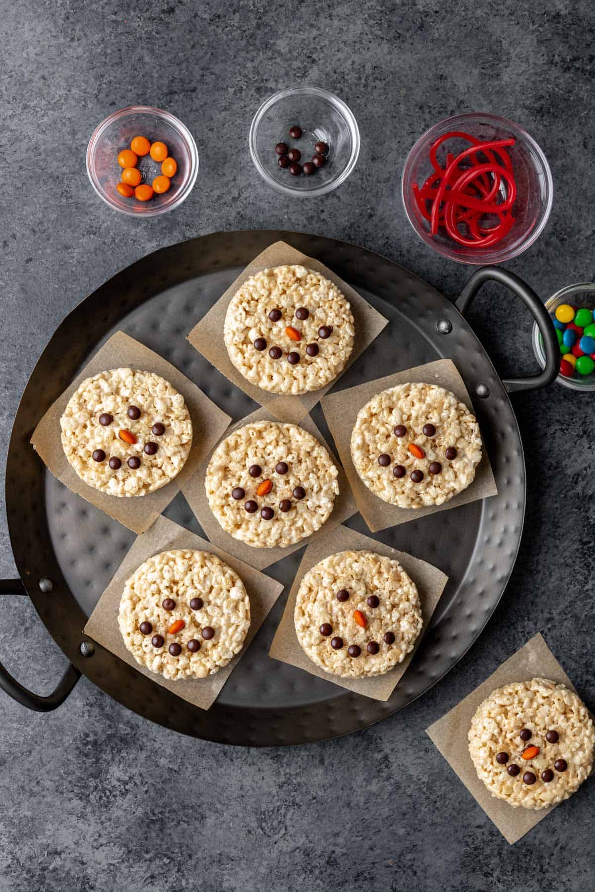 Snowman rice krispie treats with brown candy eyes and smiley faces and orange candy noses.