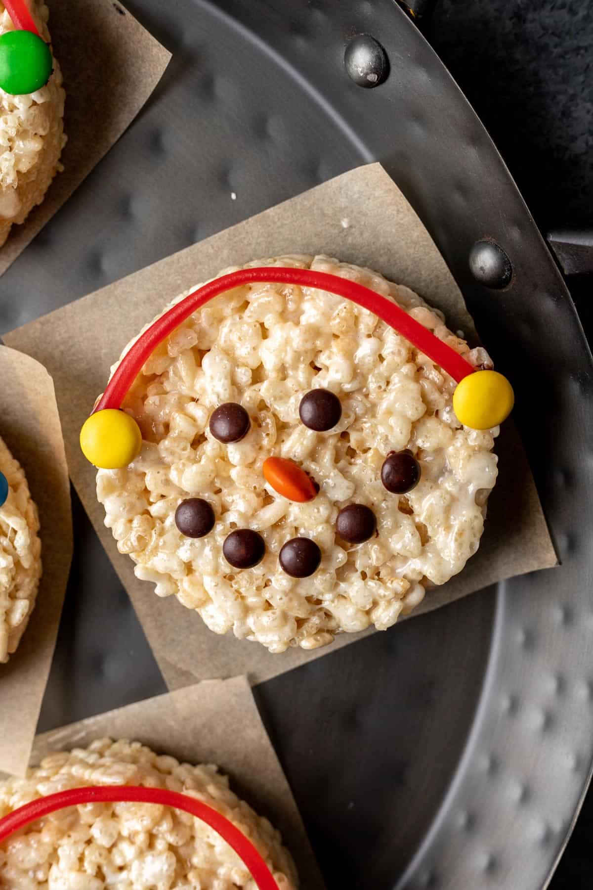 A snowman rice krispie treat with yellow candy earmuffs and an orange candy nose.