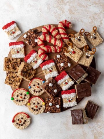 Holiday rice krispie treats dessert board with reindeer, santas, candy canes, snowmen, peanut butter, smores, and hot chocolate rice krispie treats.