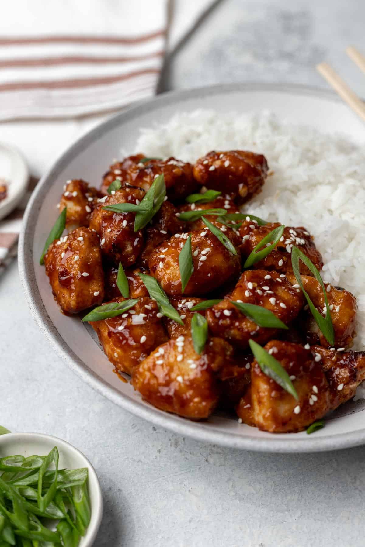 Air fryer general tso's chicken topped with green onions and sesame seeds in a gray bowl.