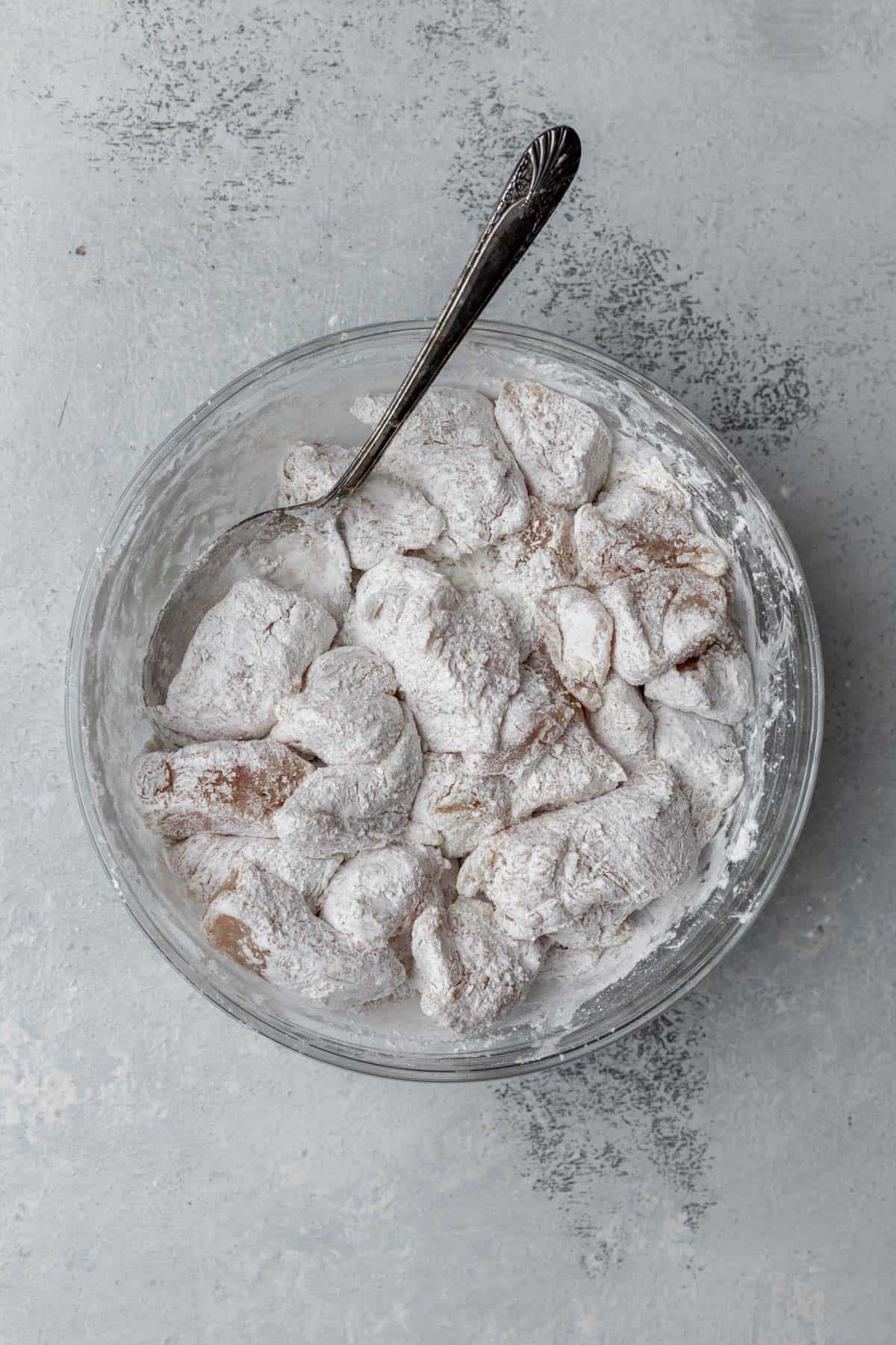 Cubed raw chicken coated in cornstarch in a bowl.