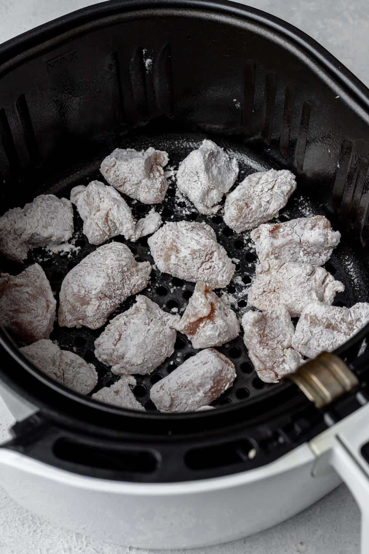 Cubed cornstarch-coated chicken in the basket of an air fryer.