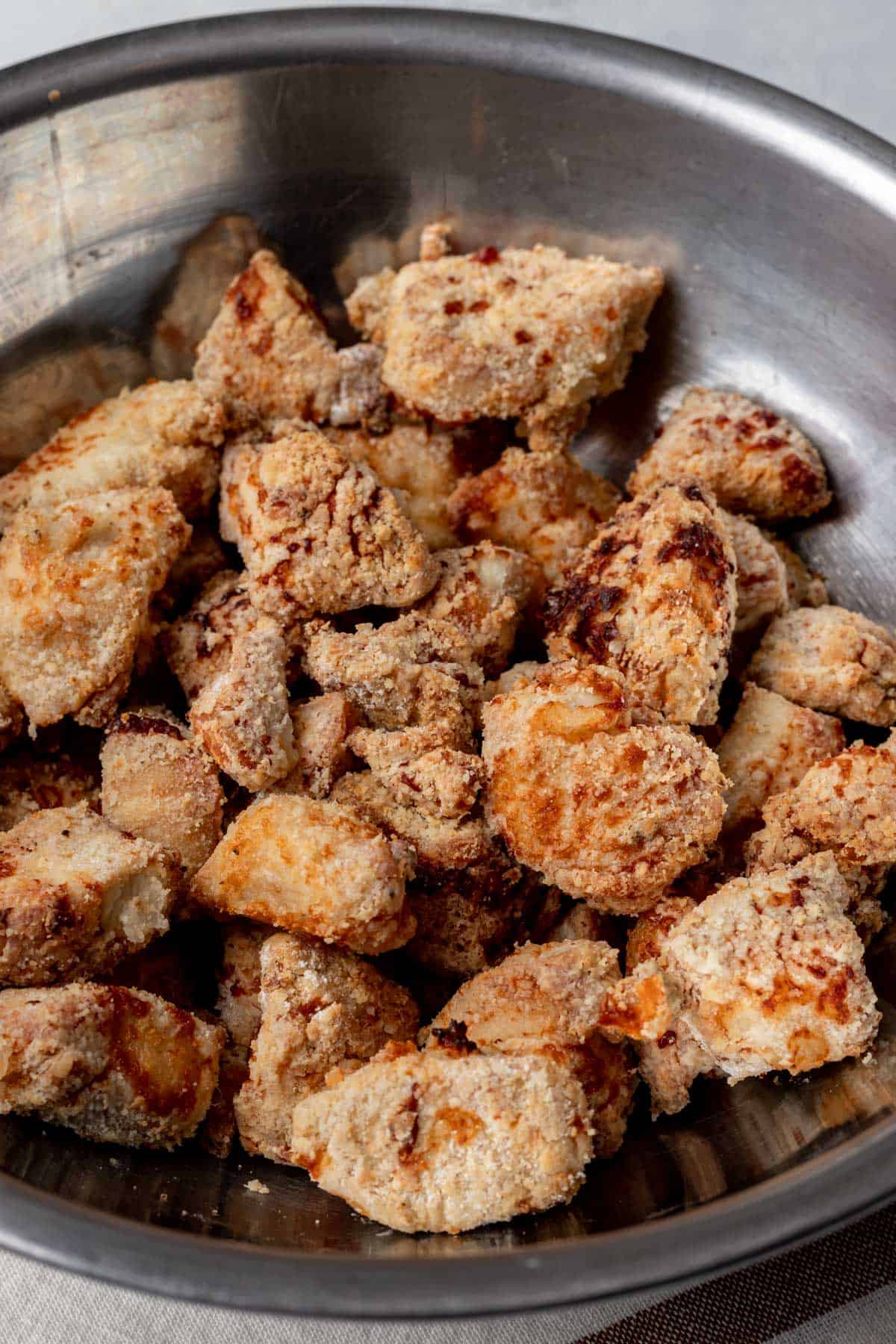 Golden brown air fryer chicken in a mixing bowl.