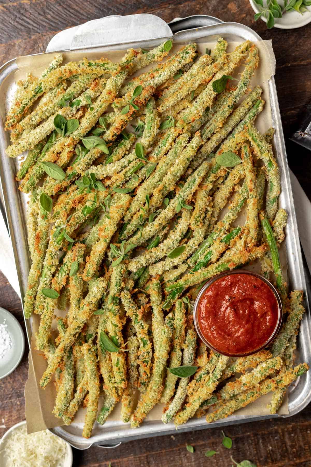 Air fryer green bean fries on a sheet tray with a side of marinara dipping sauce.
