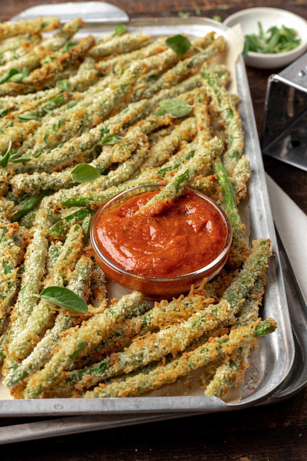 An air fryer green bean dipped in marinara sauce on a sheet tray.