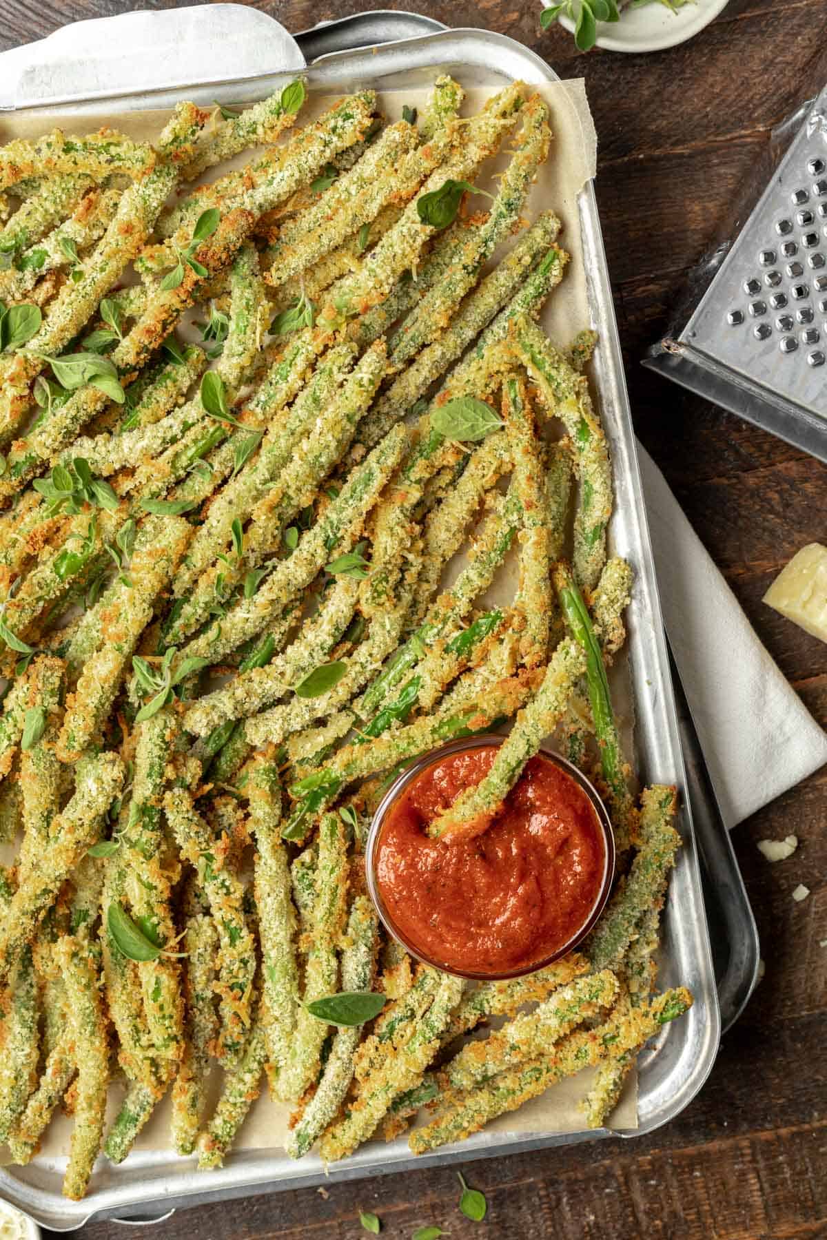 Air fryer green bean fries garnished with fresh herbs and a side of sauce on a sheet tray.