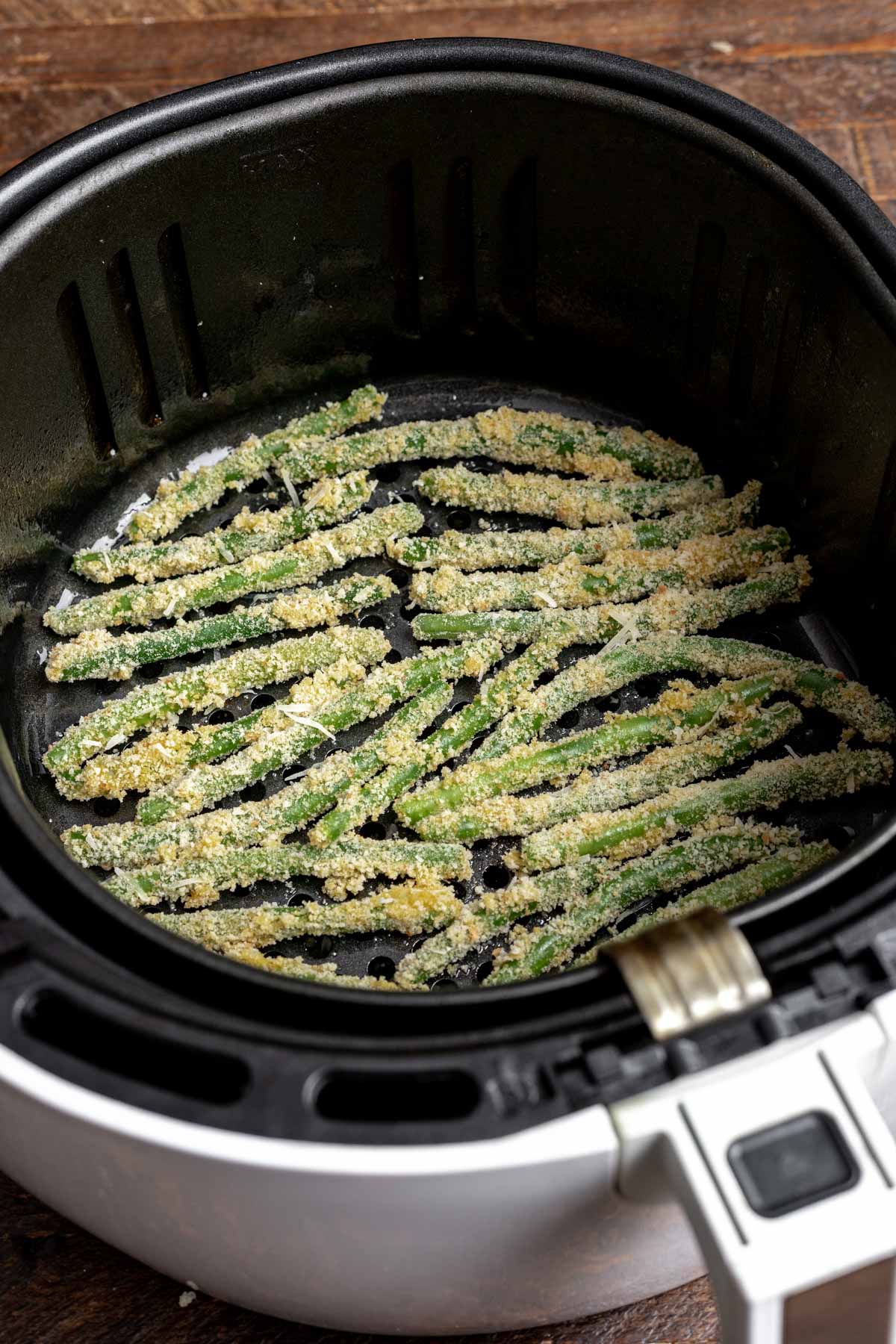 Green beans coated in breadcrumbs in an air fryer basket.