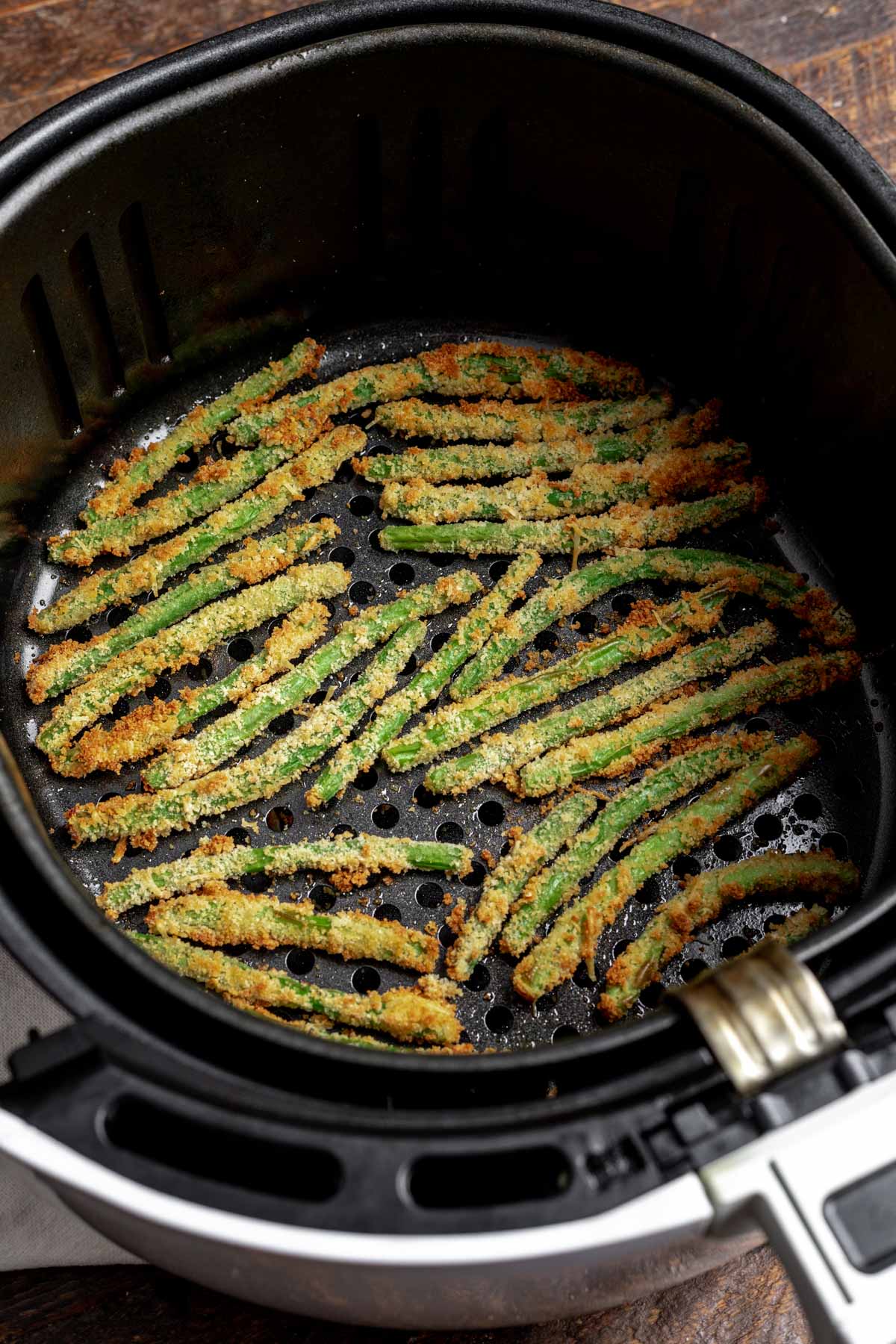 Golden brown air fryer green beans in an air fryer basket after cooking.