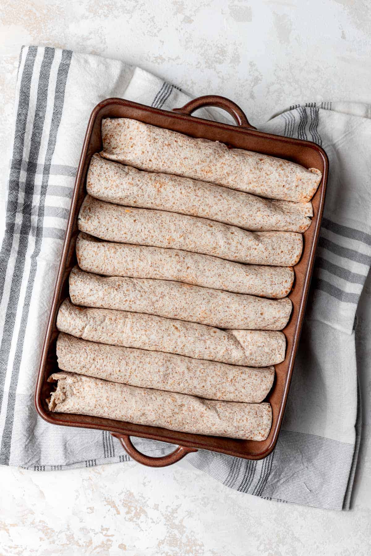 Eight rolled enchiladas in a baking dish.