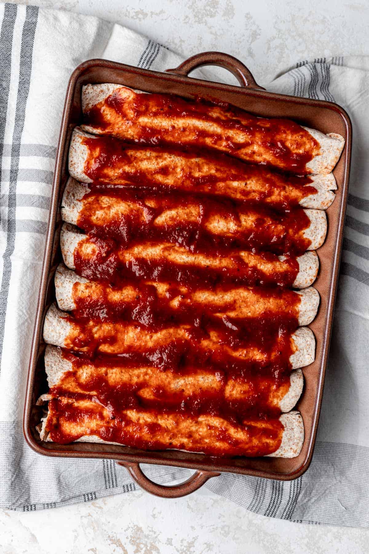 Eight rolled enchiladas topped with enchilada sauce in a baking dish.