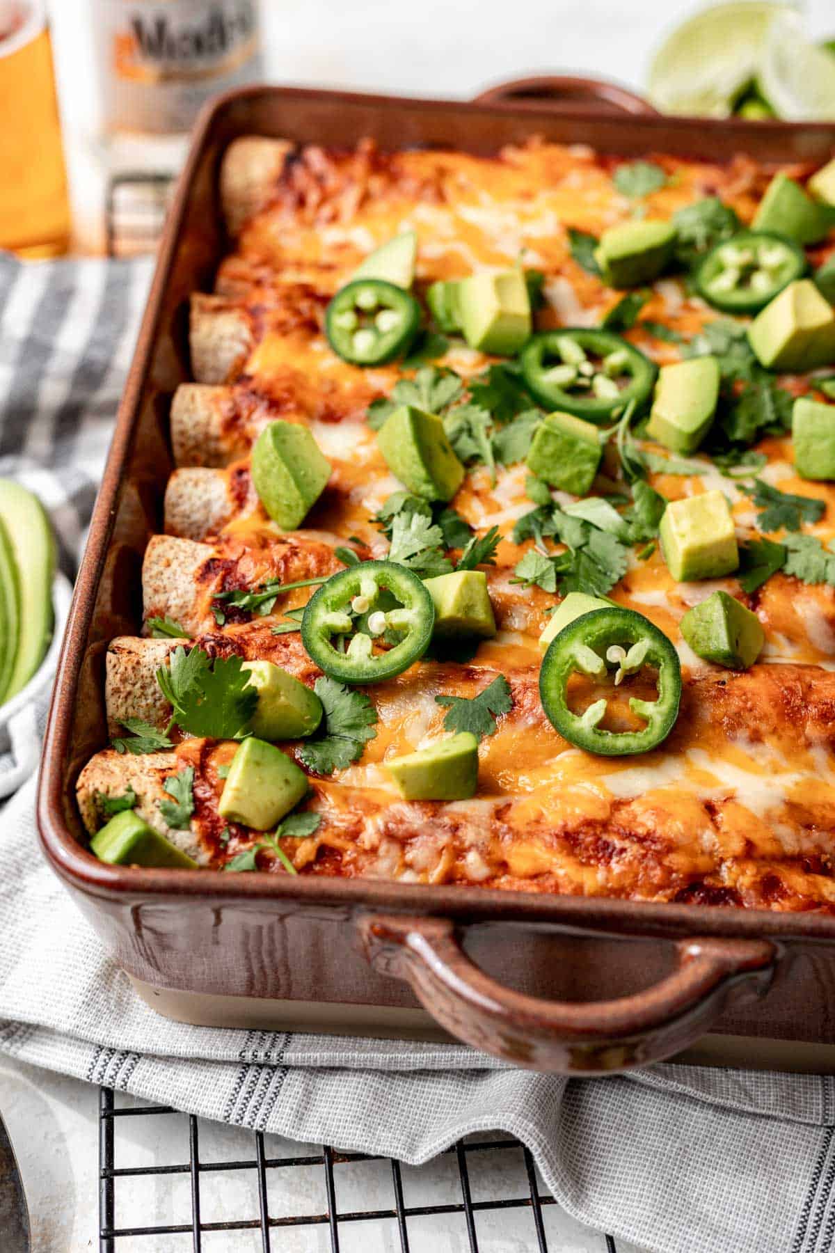 Cheesy ground turkey enchiladas in a baking dish with avocado and jalapeños on top.