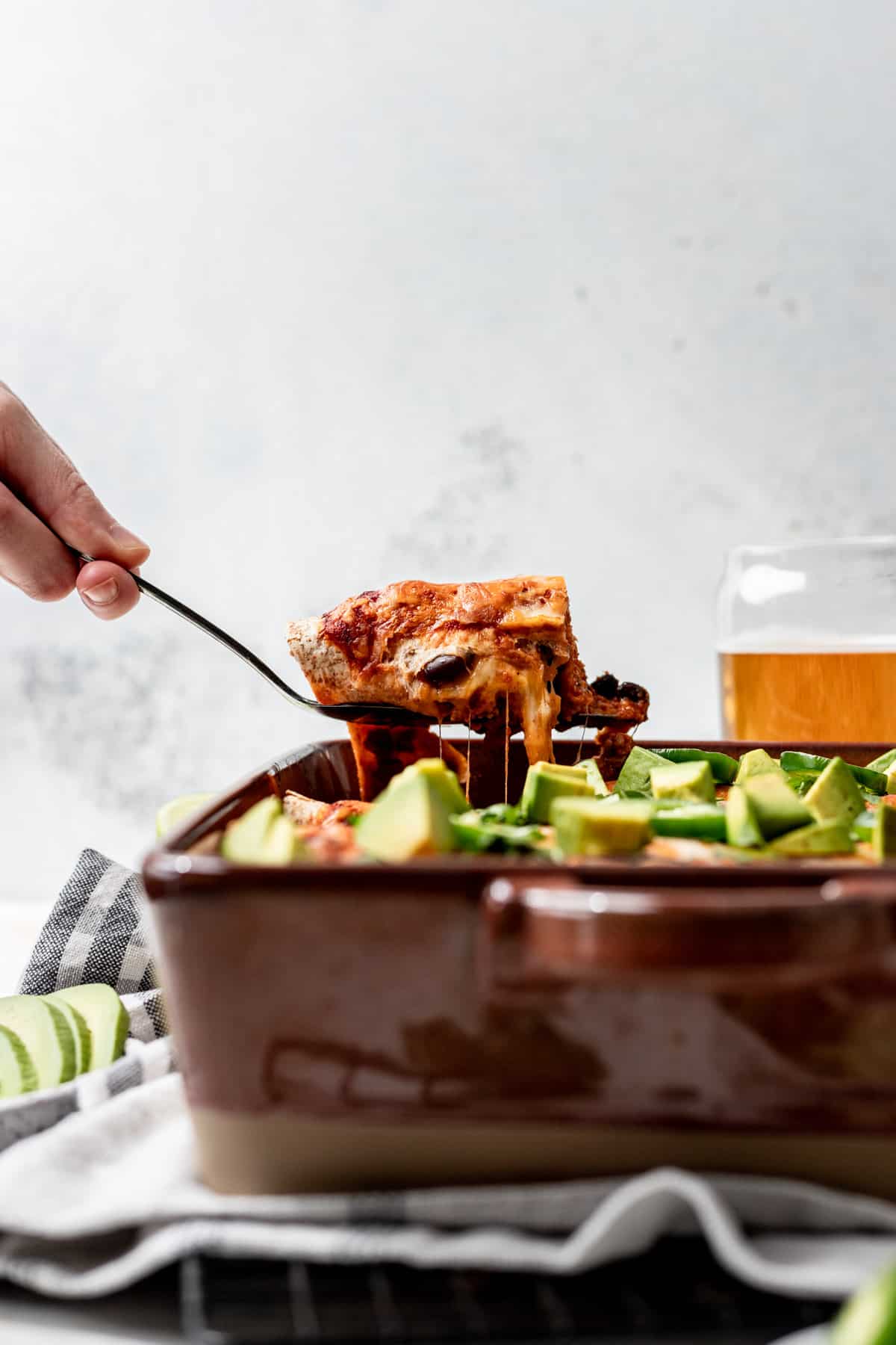 A spatula lifting cheesy ground turkey enchiladas out of the baking dish.