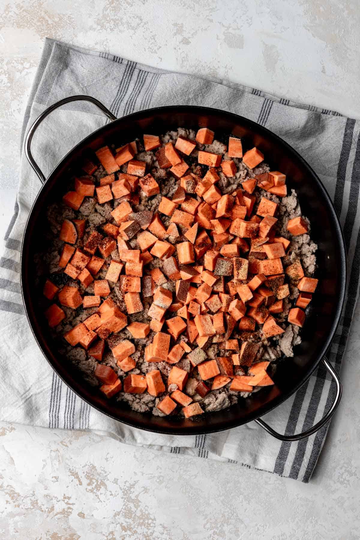Raw sweet potatoes combined with ground turkey in a skillet.
