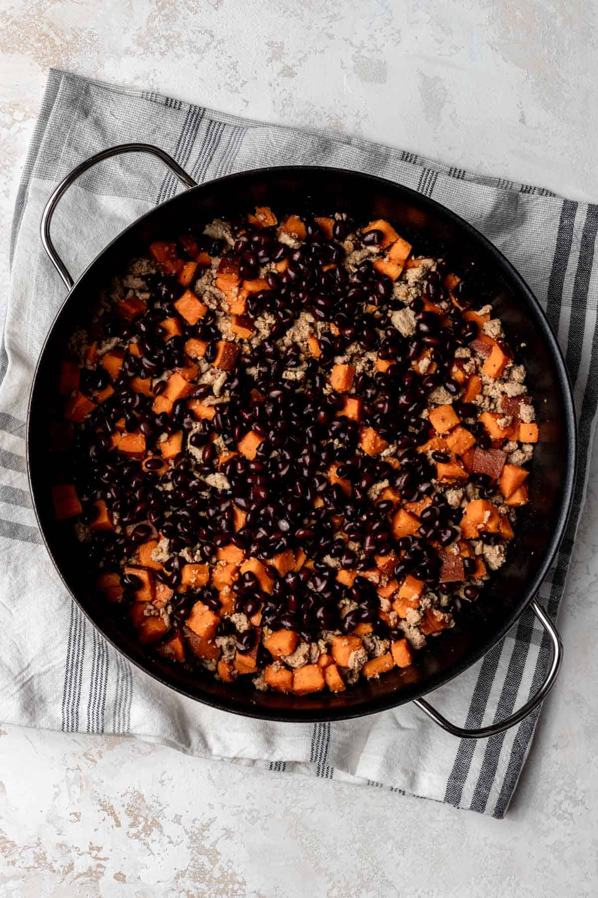Black beans mixed with ground turkey and sweet potato in a skillet.