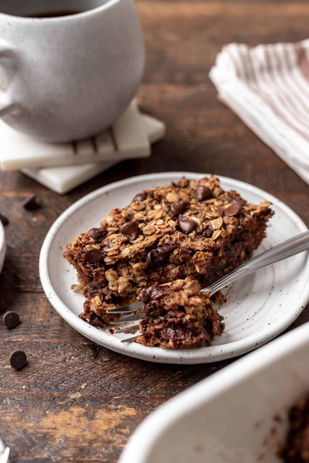 A slice of chocolate baked oats on a white plate with a fork.