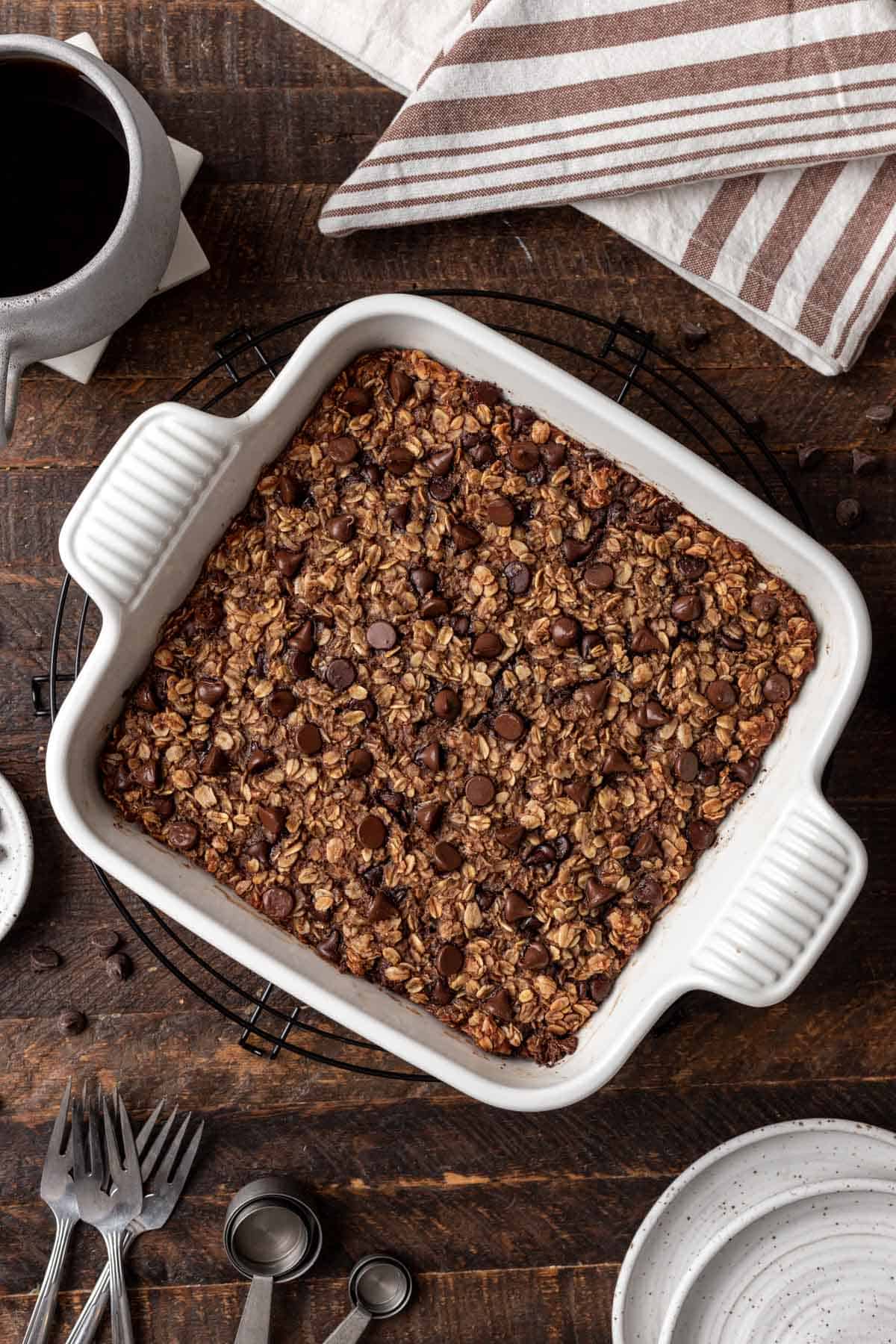 Cooked chocolate baked oatmeal in a white dish with a cup of coffee next to it.