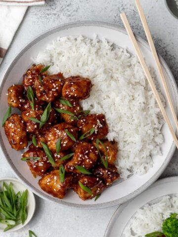 Air fryer general tso's chicken in a bowl with white rice and chopsticks.