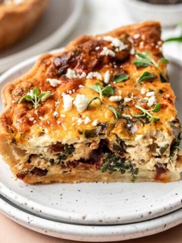 A slice of mediterranean sun-dried tomato quiche on a white plate.