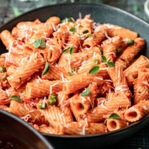 Pink sauce pasta in a green bowl with shredded parmesan cheese and fresh herbs on top.