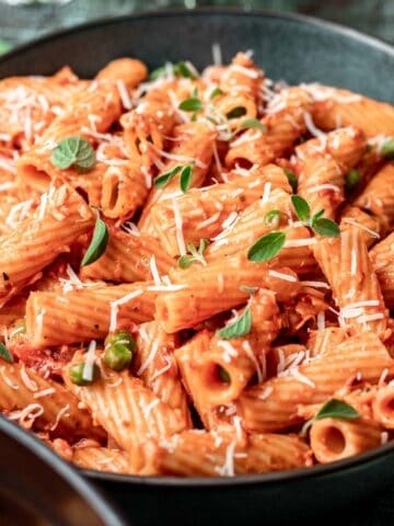 Pink sauce pasta in a green bowl with shredded parmesan cheese and fresh herbs on top.