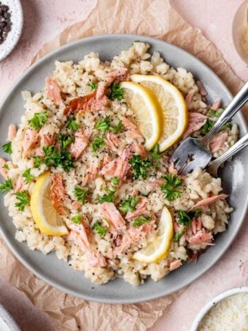 Risotto topped with smoked salmon, sliced lemons, and fresh parsley.