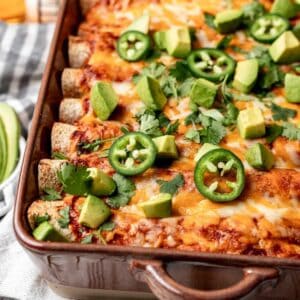 Ground turkey enchiladas in a baking dish with avocado and jalapeños on top.