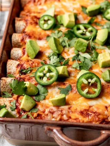 Ground turkey enchiladas in a baking dish with avocado and jalapeños on top.