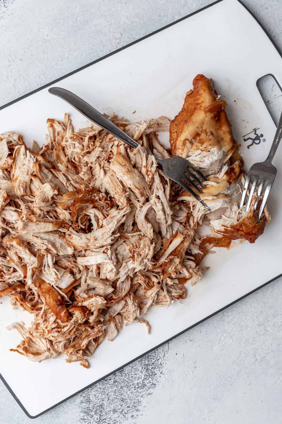 Chicken on a cutting board shredded with two forks.