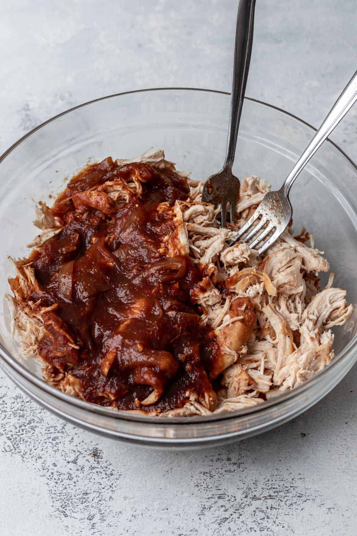 Shredded chicken in a mixing bowl with bbq sauce.
