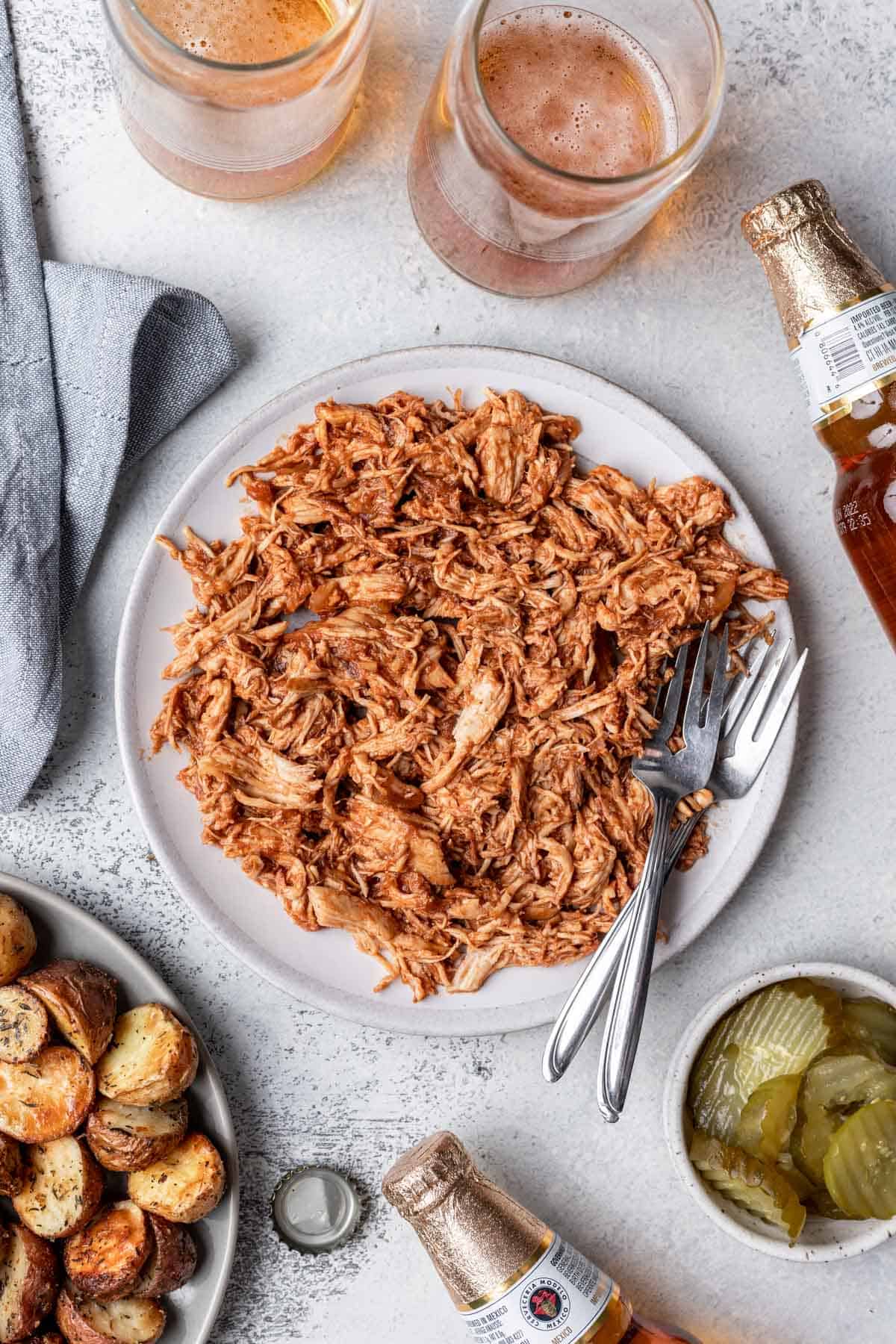 Instant pot bbq pulled chicken on a plate with two forks and a side of pickles.