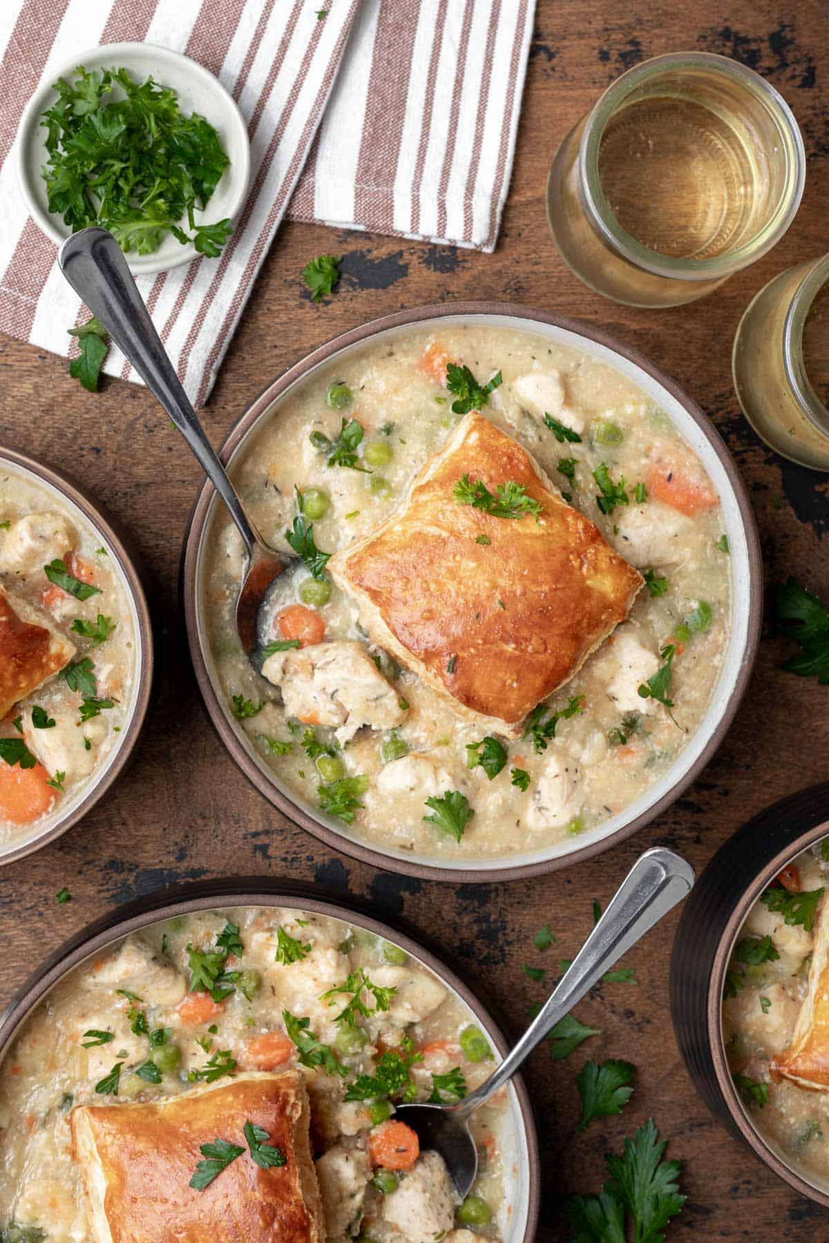 4 bowls of instant pot chicken pot pie topped with a puff pastry crust and serving spoons.