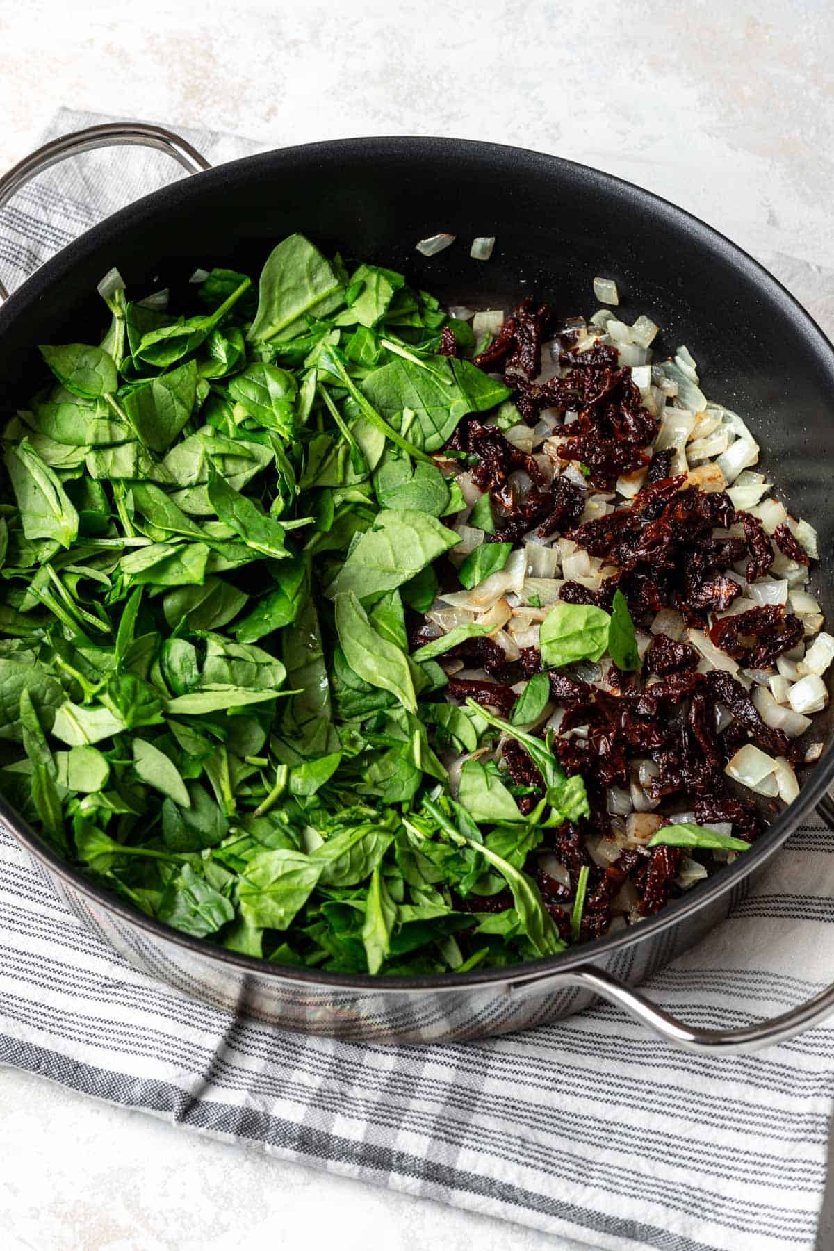 Spinach, sun-dried tomatoes, and onion in a skillet.