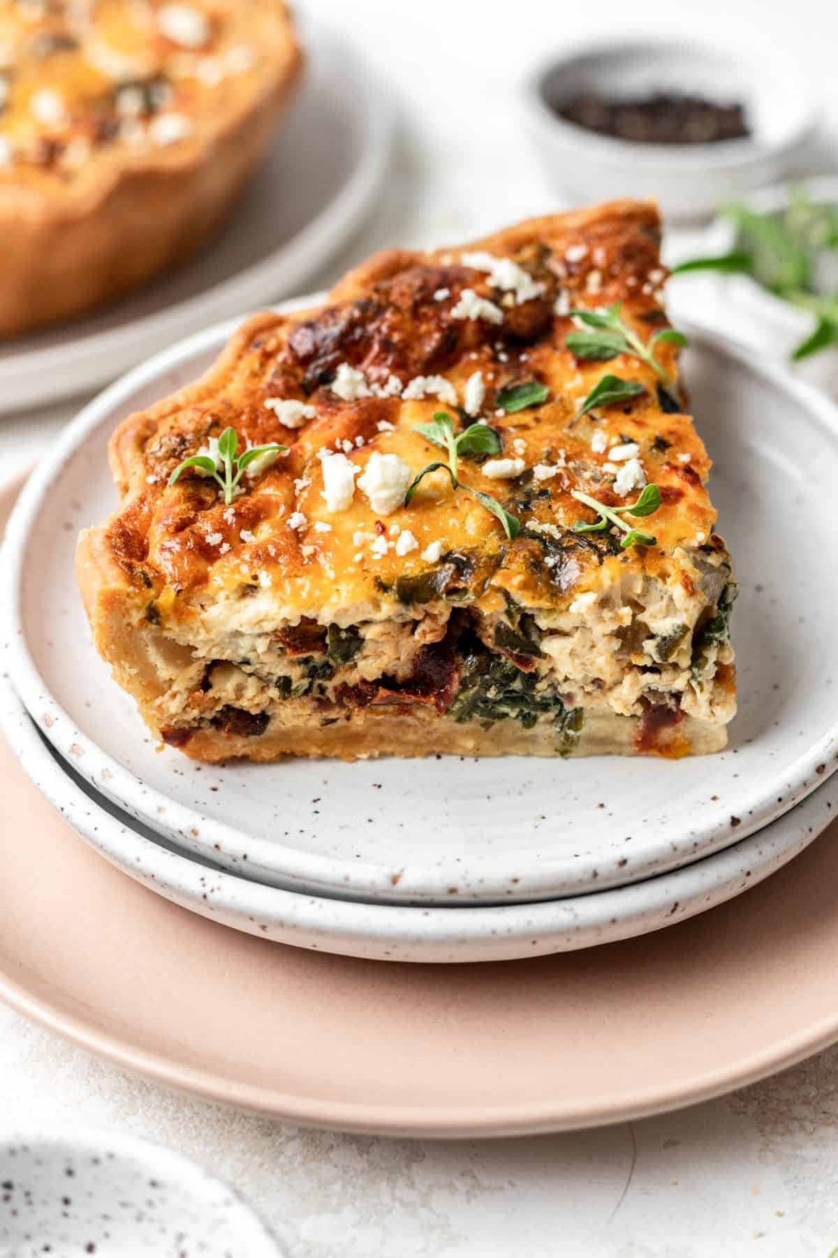 A slice of mediterranean sun-dried tomato quiche on a white plate.