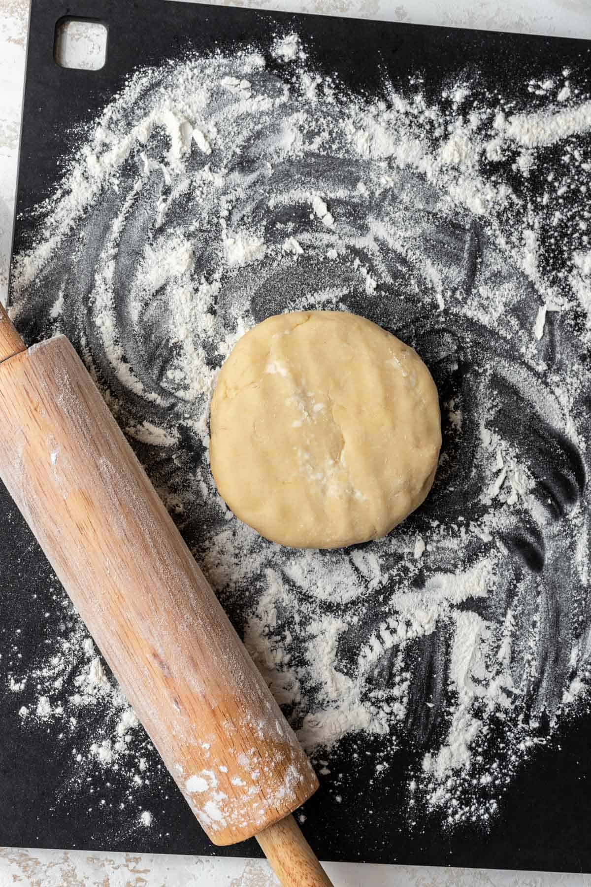 A disc of quiche dough on a floured cutting board with a rolling pin.