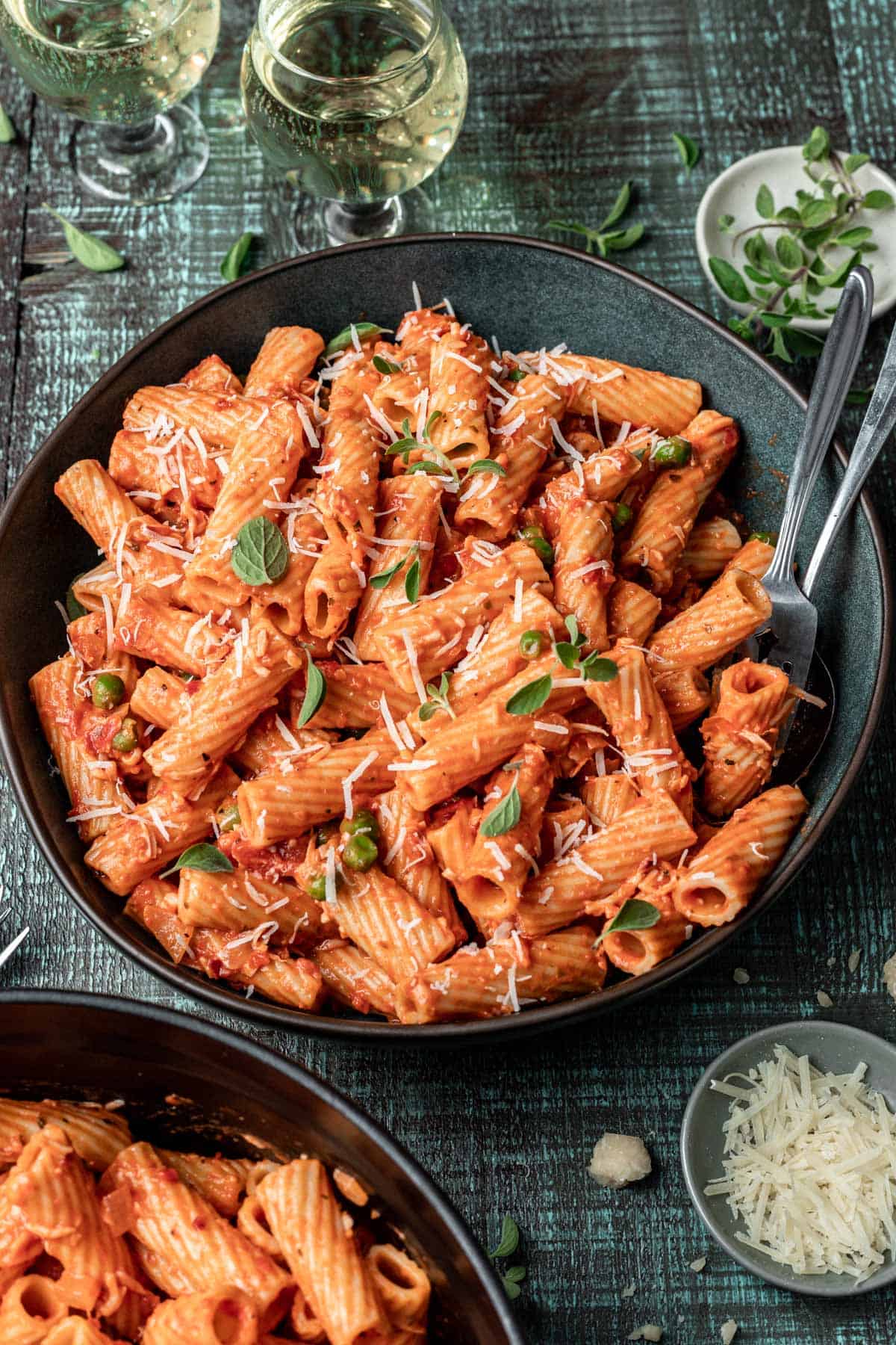 A bowl of pink sauce pasta with two forks and a glass of wine.