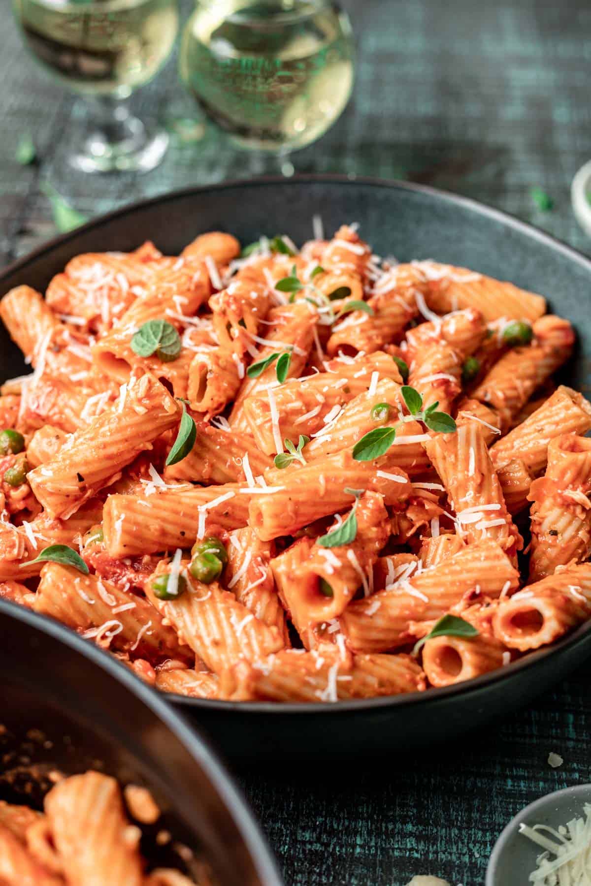 Pink sauce pasta in a green bowl with shredded parmesan cheese and fresh herbs on top.