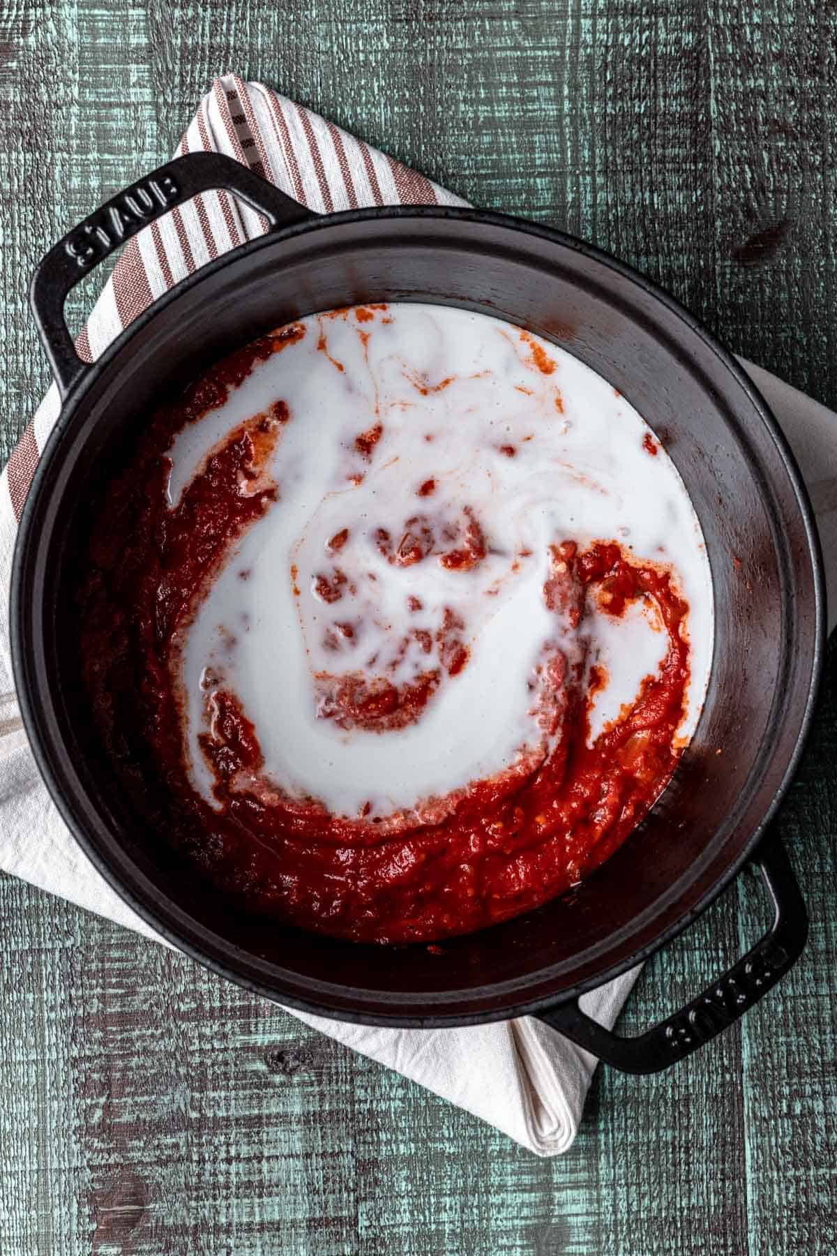 Tomato sauce mixed with coconut cream in a black pot.