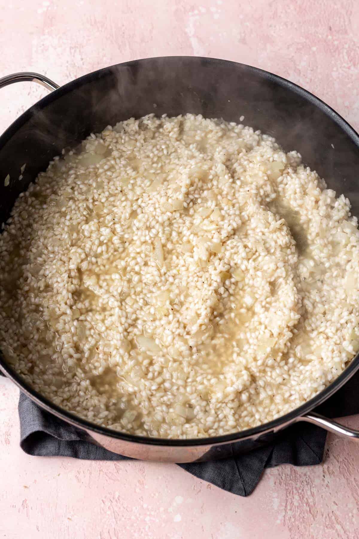 Broth slowly getting absorbed by the rice in a large skillet.